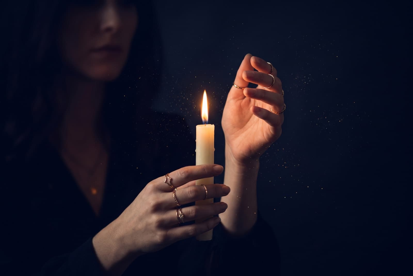 Manos con anillos dorados sostienen una vela encendida en la oscuridad.